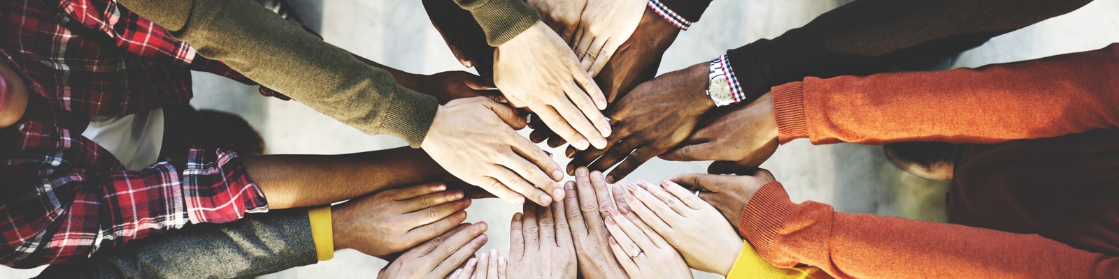 Group of diverse people holding their hands into the center of a circle.