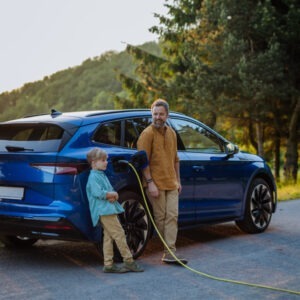 A father and son leaning against an electrical car while it is charging.